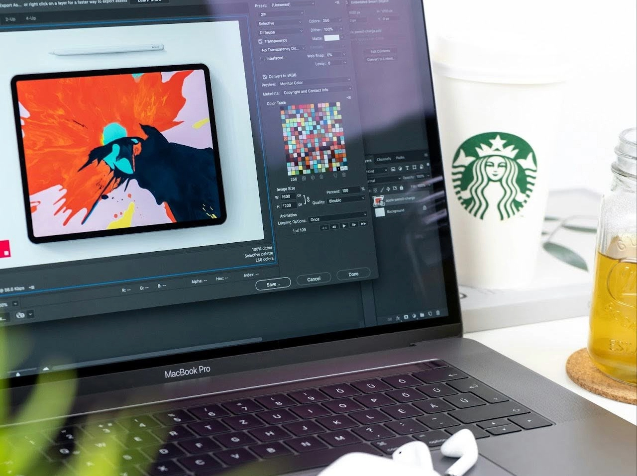 MacBook Pro displaying digital artwork with Adobe Photoshop, alongside a pair of AirPods and a Starbucks cup, symbolizing creativity and focus in a modern workspace, as featured on the WorkBuzz blog.