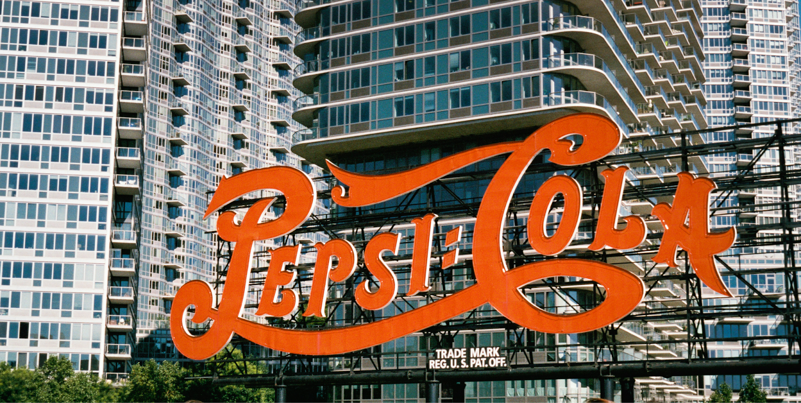 The Iconic Pepsi-Cola sign in front of modern high-rise buildings. The image symbolizes the blend of classic branding with contemporary urban development, as featured on the WorkBuzz blog.